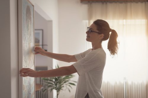 Woman,Hanging,A,Painting,At,Home,And,Decorating,Her,Contemporary Woman,Hanging,A,Painting,At,Home,And,Decorating,Her,Contemporary