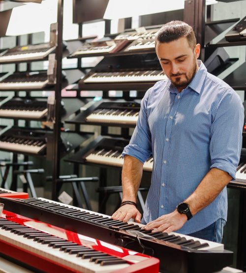 Young,Bearded,Man,Choosing,Electric,Piano,Or,Synthesizer,In,A